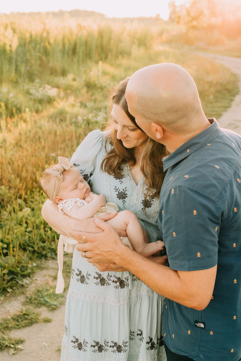 Family Photographer, a mother and father hold their new baby outside