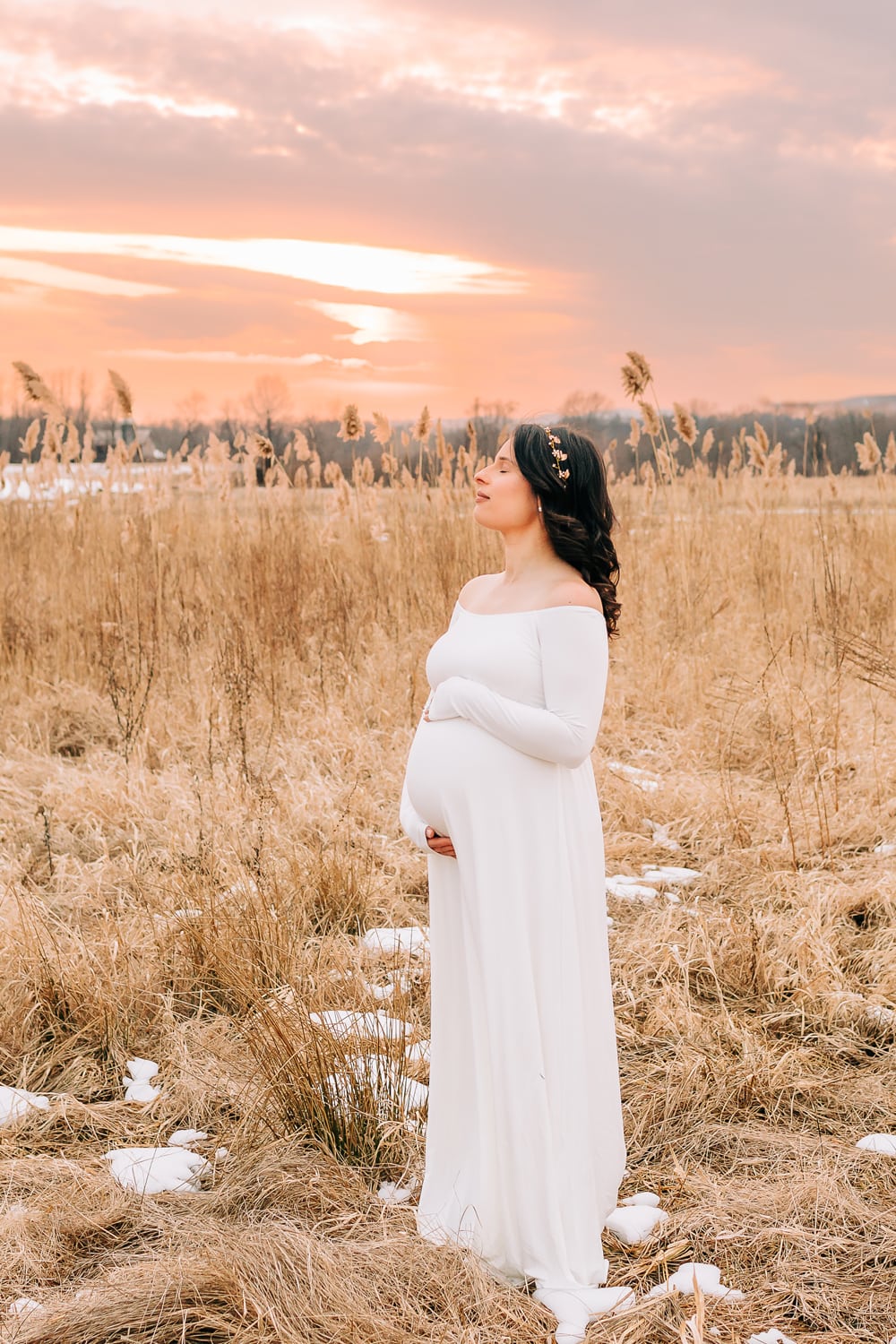 Maternity Photographer, a pregnant woman is standing in a field at sunset holding her belly